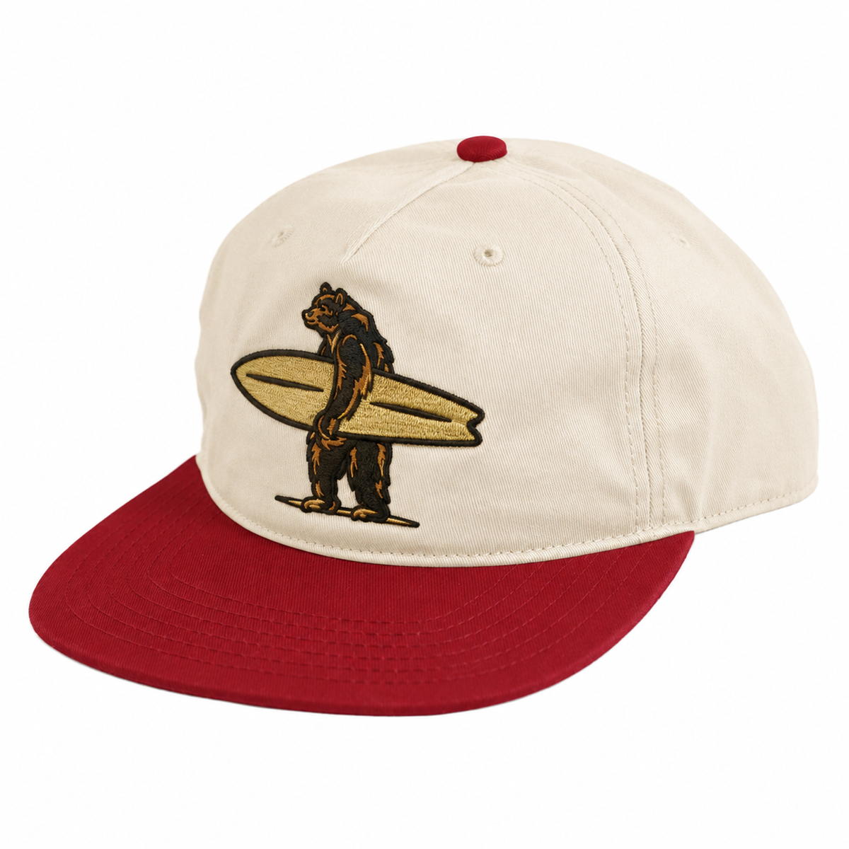 Red and cream colored chino twill snapback hat with a 3D embroidered logo of a bear holding a surfboard on the front of the hat.