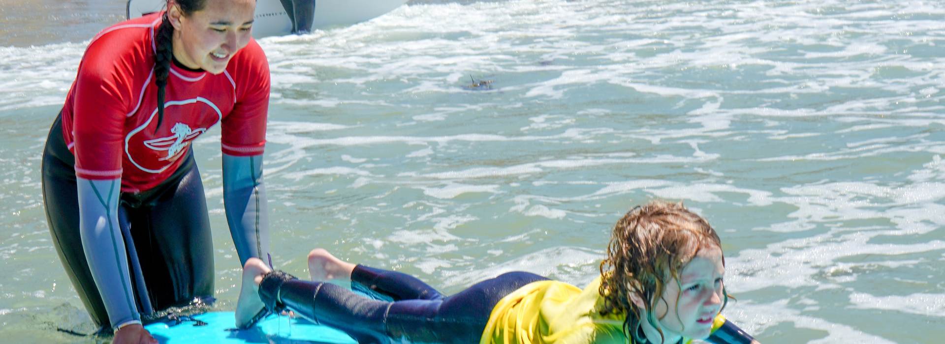 Surf instructor helping an Everyday California camper paddle into waves in the La Jolla surf
