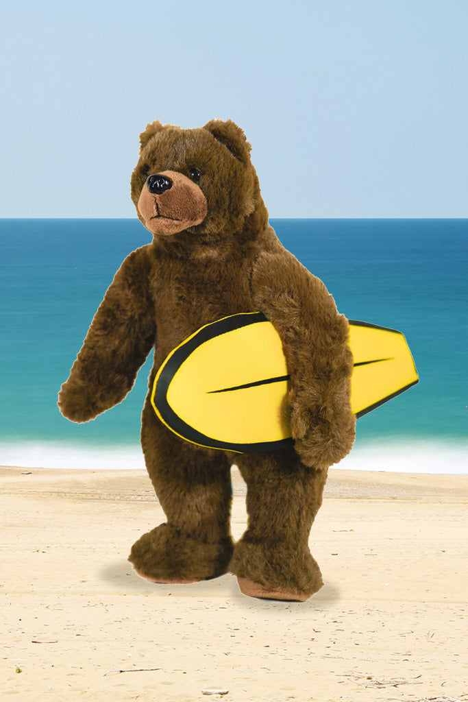 Plush bear with a yellow surfboard on a beach