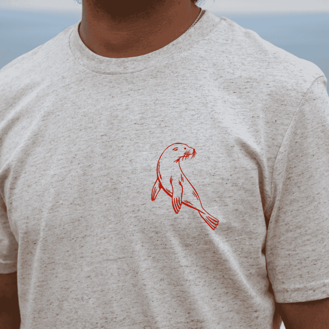 Person wearing a light gray t-shirt with a red seal graphic on a blurred natural background