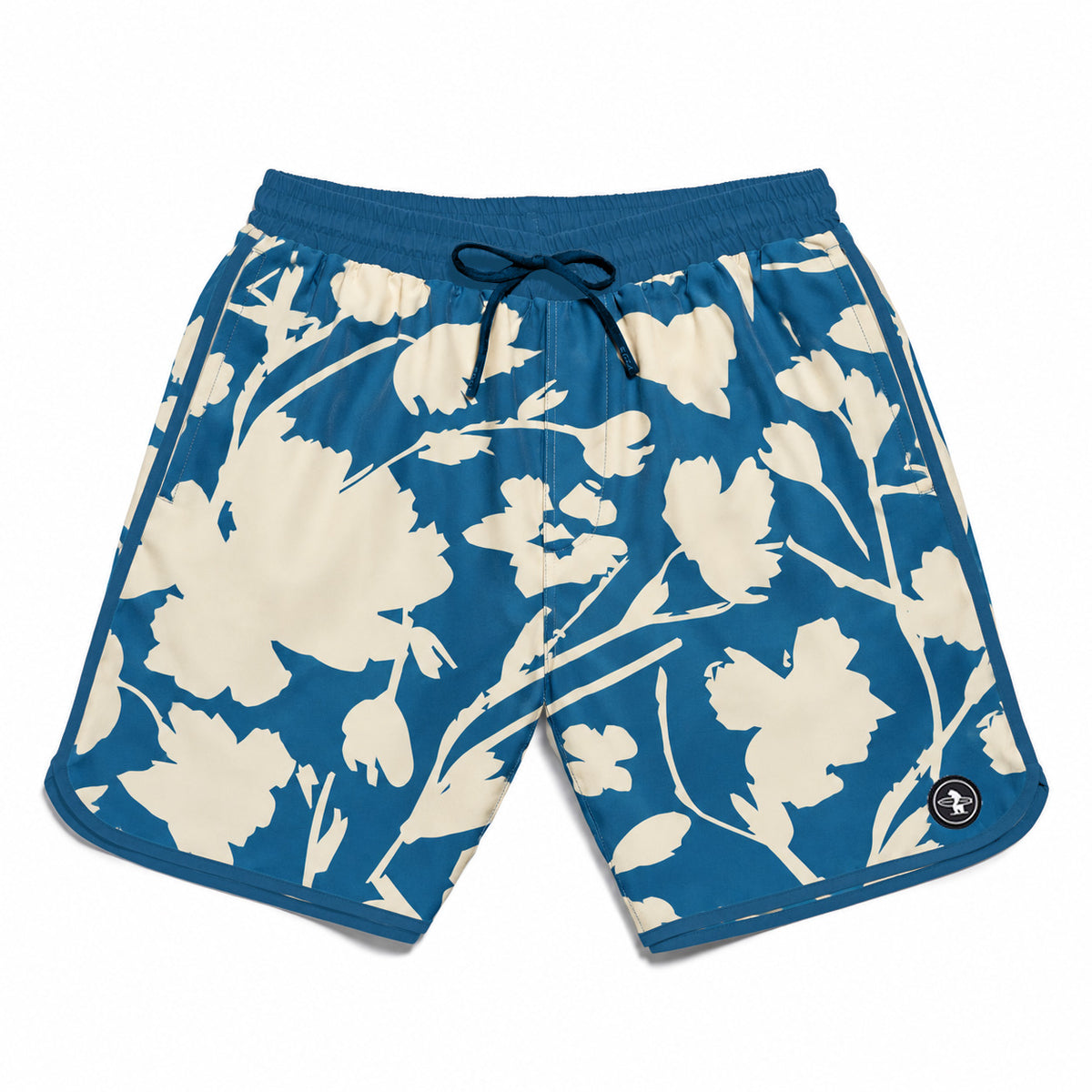 Blue and cream floral print swim trunks with a dark blue drawstring waist and a small circular logo patch on the lower left hem, shown flat on a white background.