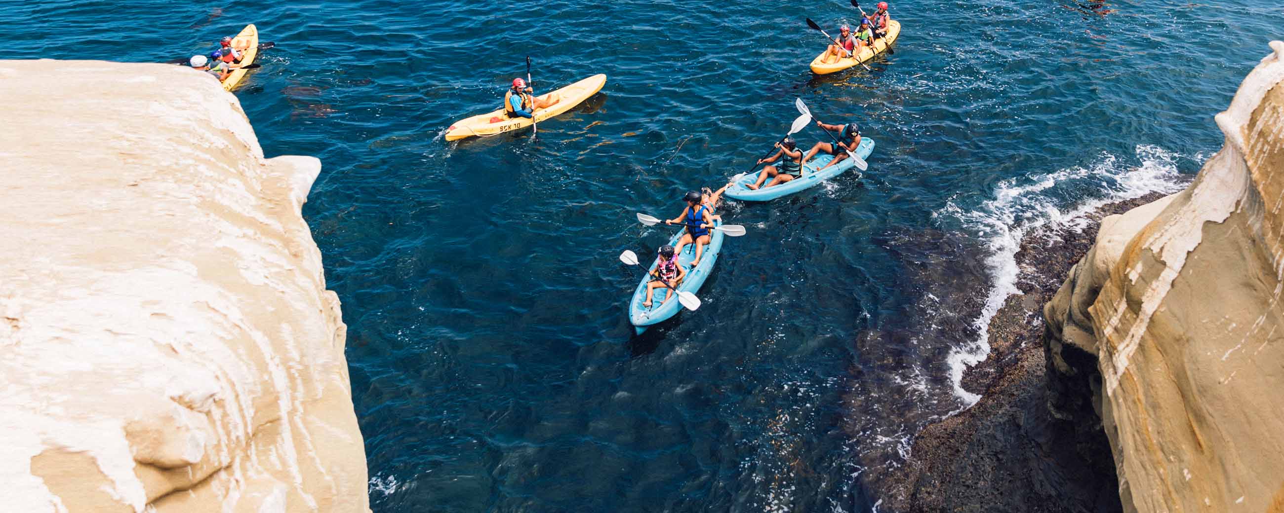 Five groups of kayakers paddling into one of the Seven Sea Caves in La Jolla with the company Everyday California.