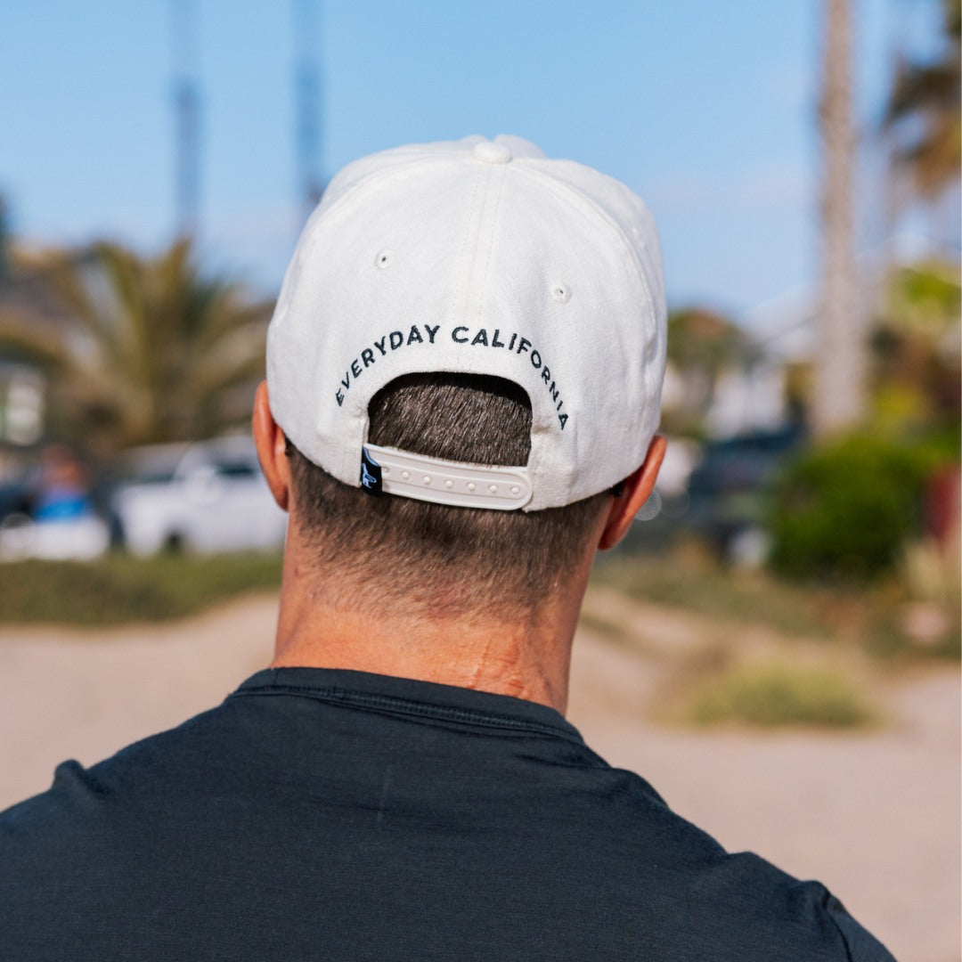 Person wearing a white cap with 'Everyday California' text, standing outdoors.