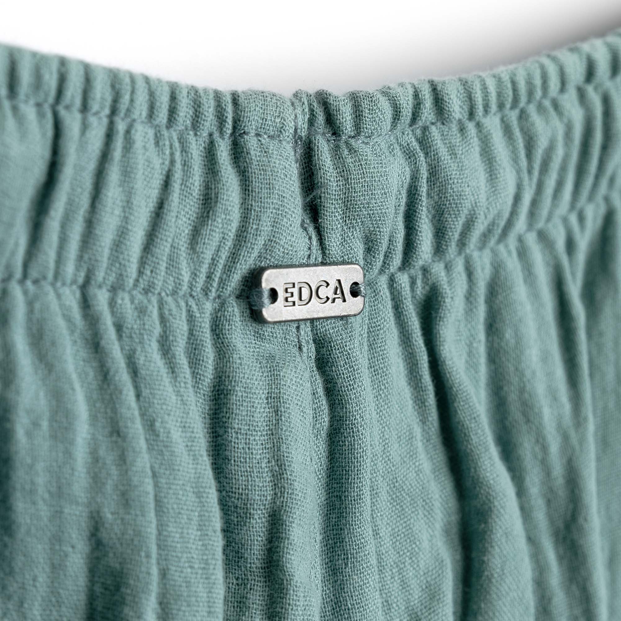 Close-up of teal fabric with a metal tag labeled 'EDCA' on a white background
