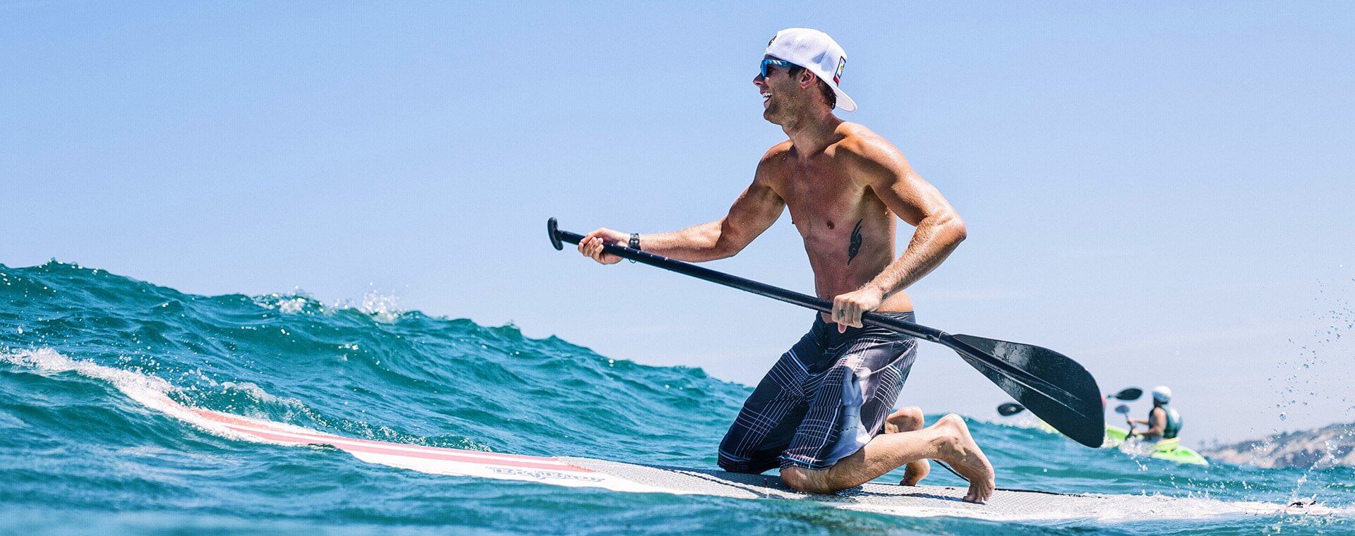 SUP Lessons in La Jolla California with Everyday California. A man kneeling on his paddle board lesson out in the water going over a wave on a sunny day. 