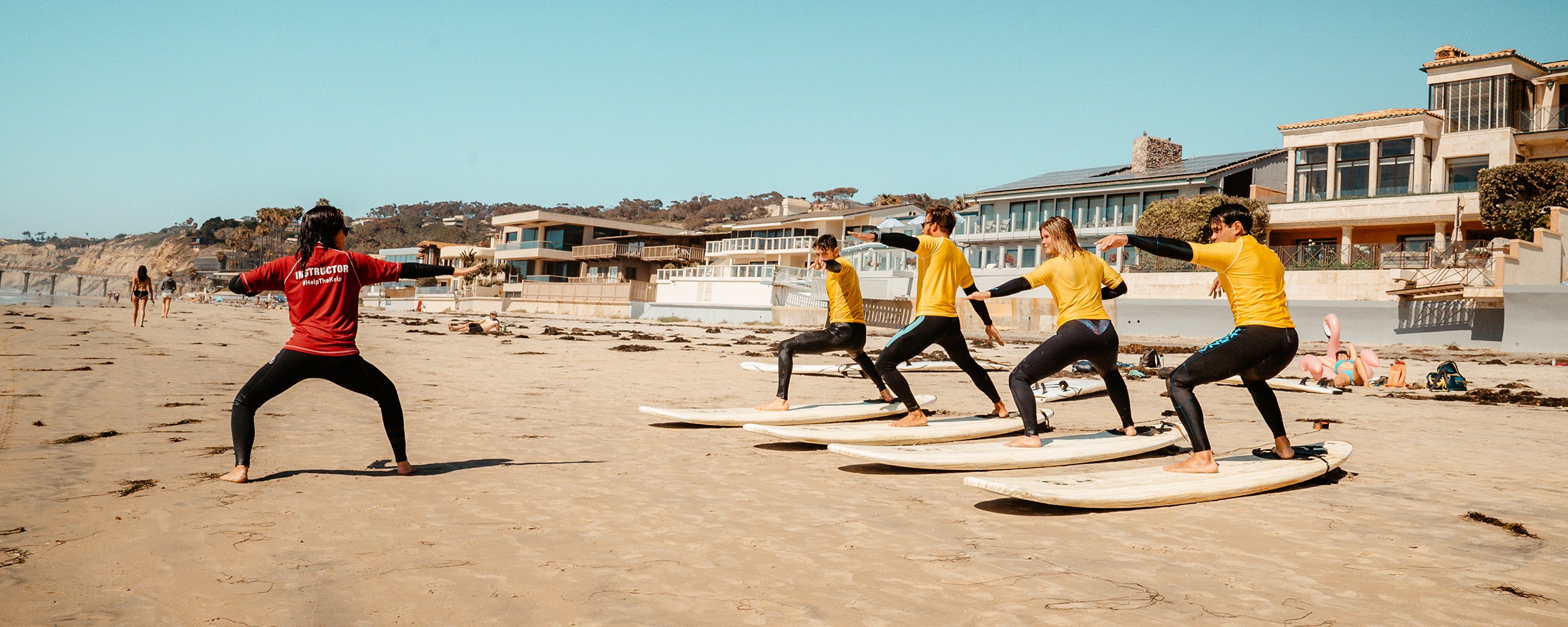 A group getting ready for the water practicing pop-ups on their board in La Jolla, California with a private surfing lesson with Everyday California.
