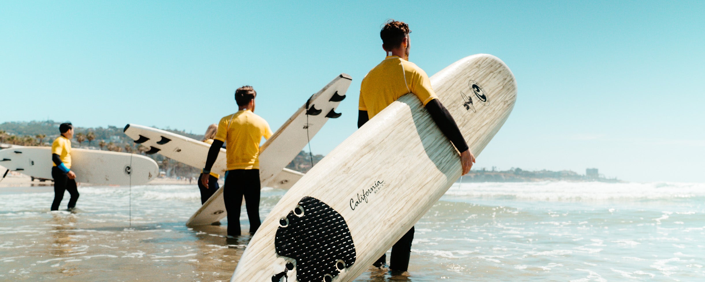 Rentals - Everyday California Surfboard Rentals. A group of surfers about to go out on a long board in San DIego, California