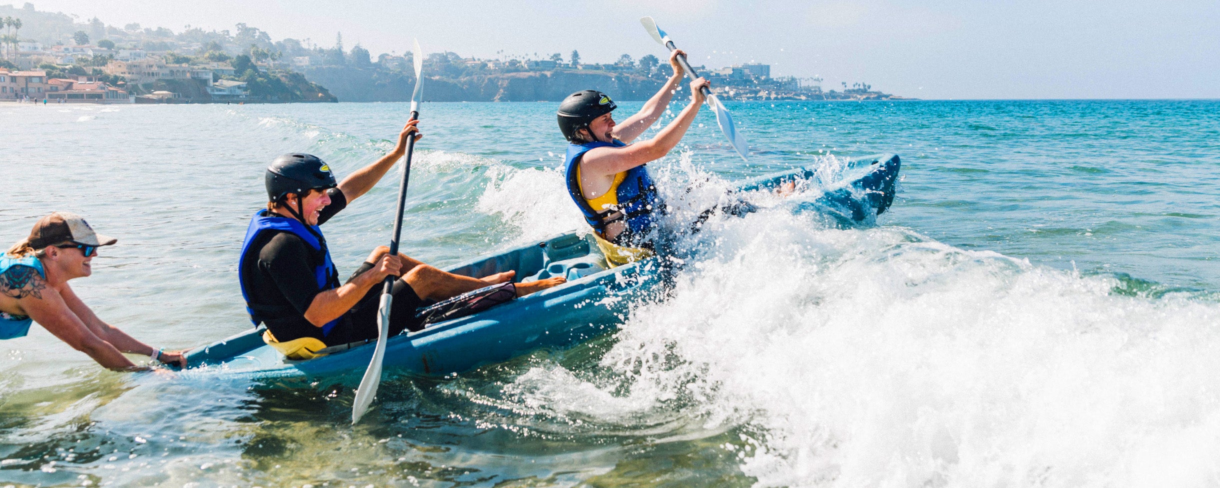 Two kayakers on a Sea Cave Kayak Tour with Everyday California, being pushed over the top of a small wave by a tour guide. They are laughing and having fun.