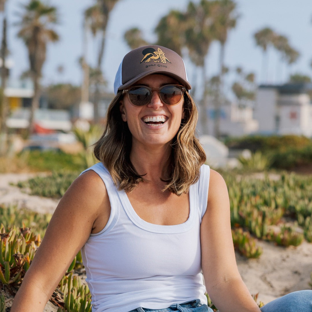 Woman wearing a cap and sunglasses, sitting outdoors with palm trees in the background