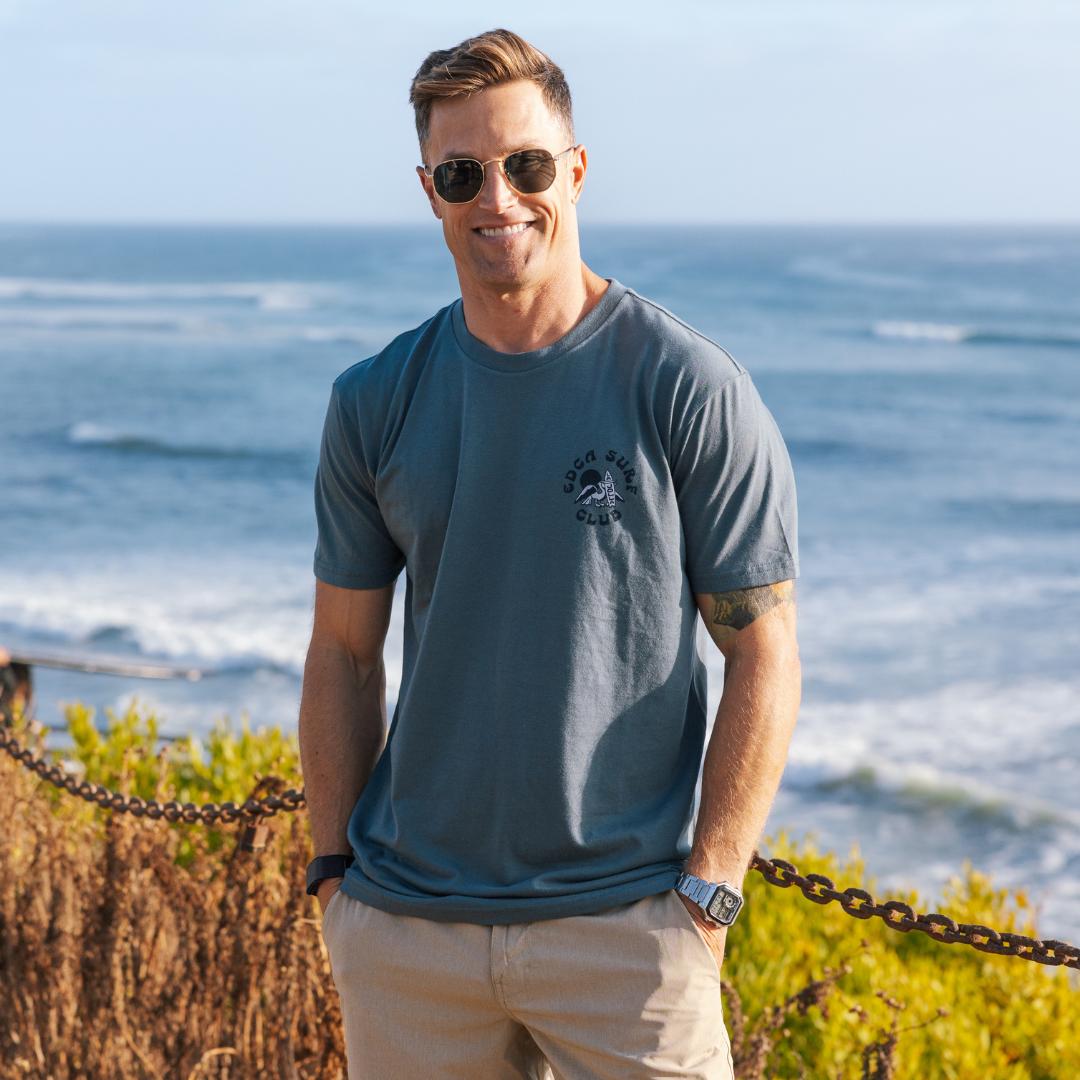 Man wearing sunglasses and a blue t-shirt standing by the ocean
