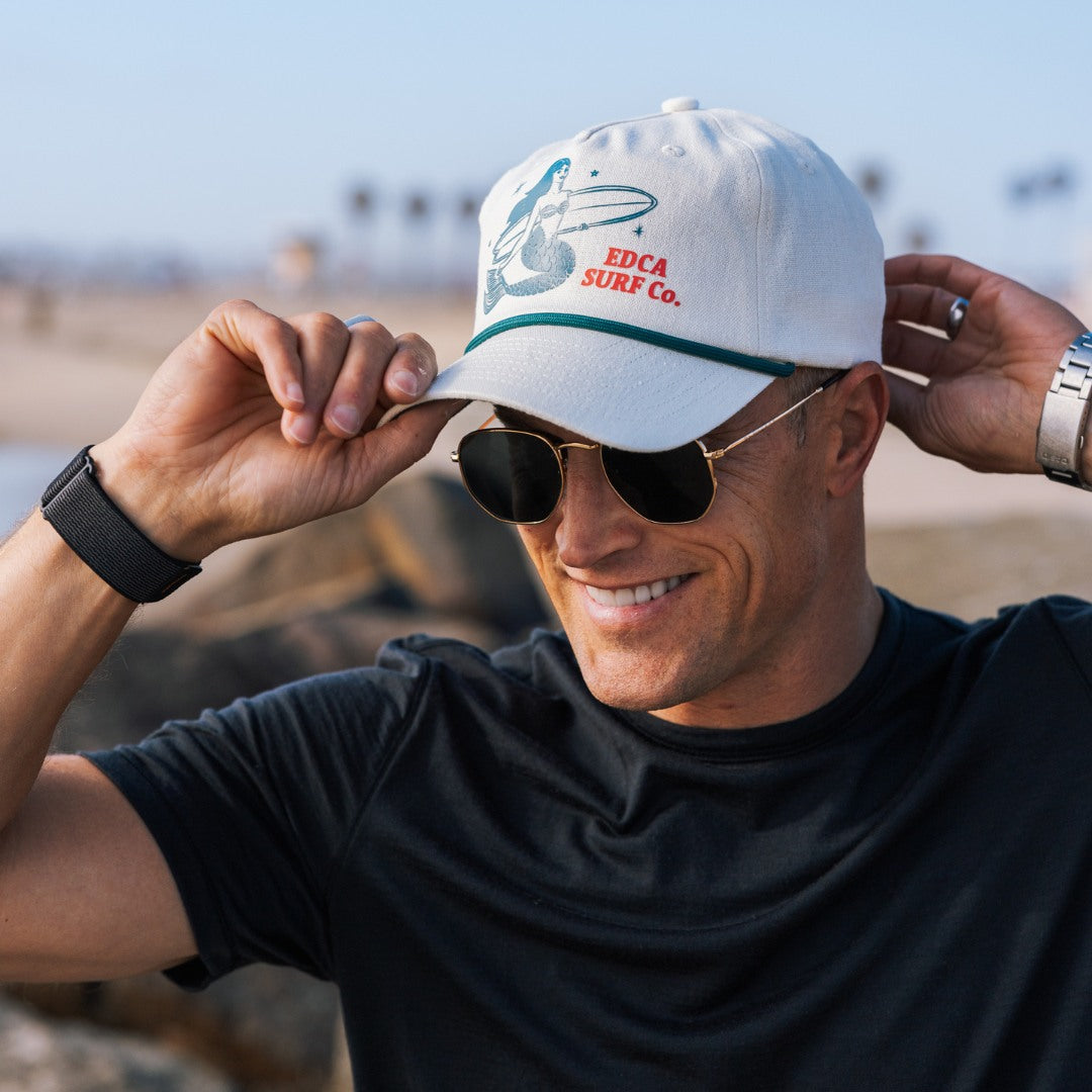 Man wearing a white cap with branding and sunglasses, standing outdoors.