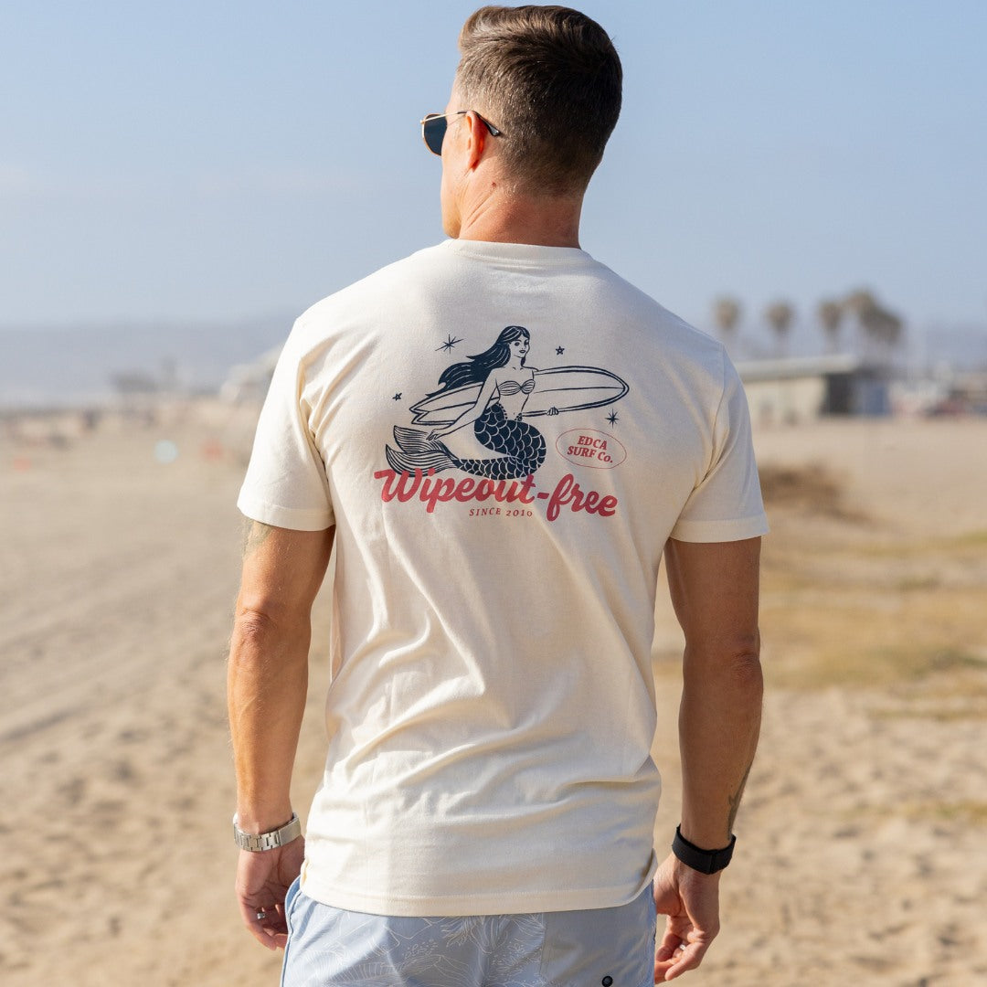 Man wearing a t-shirt with a mermaid graphic and 'Wipeout Free' text on a beach.