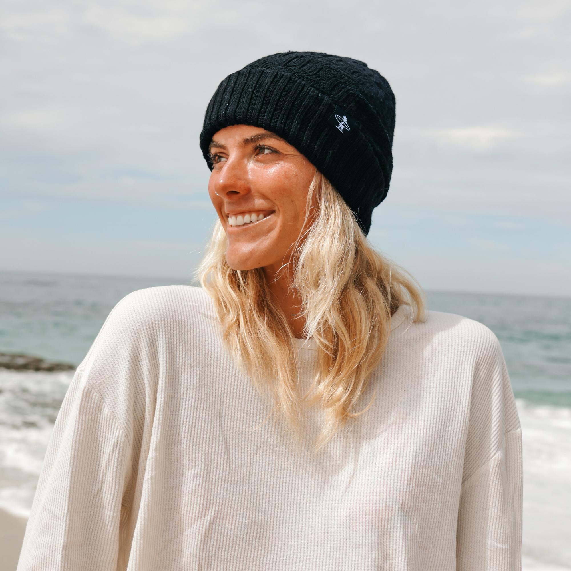 Woman wearing a black knit beanie and white sweater by the ocean