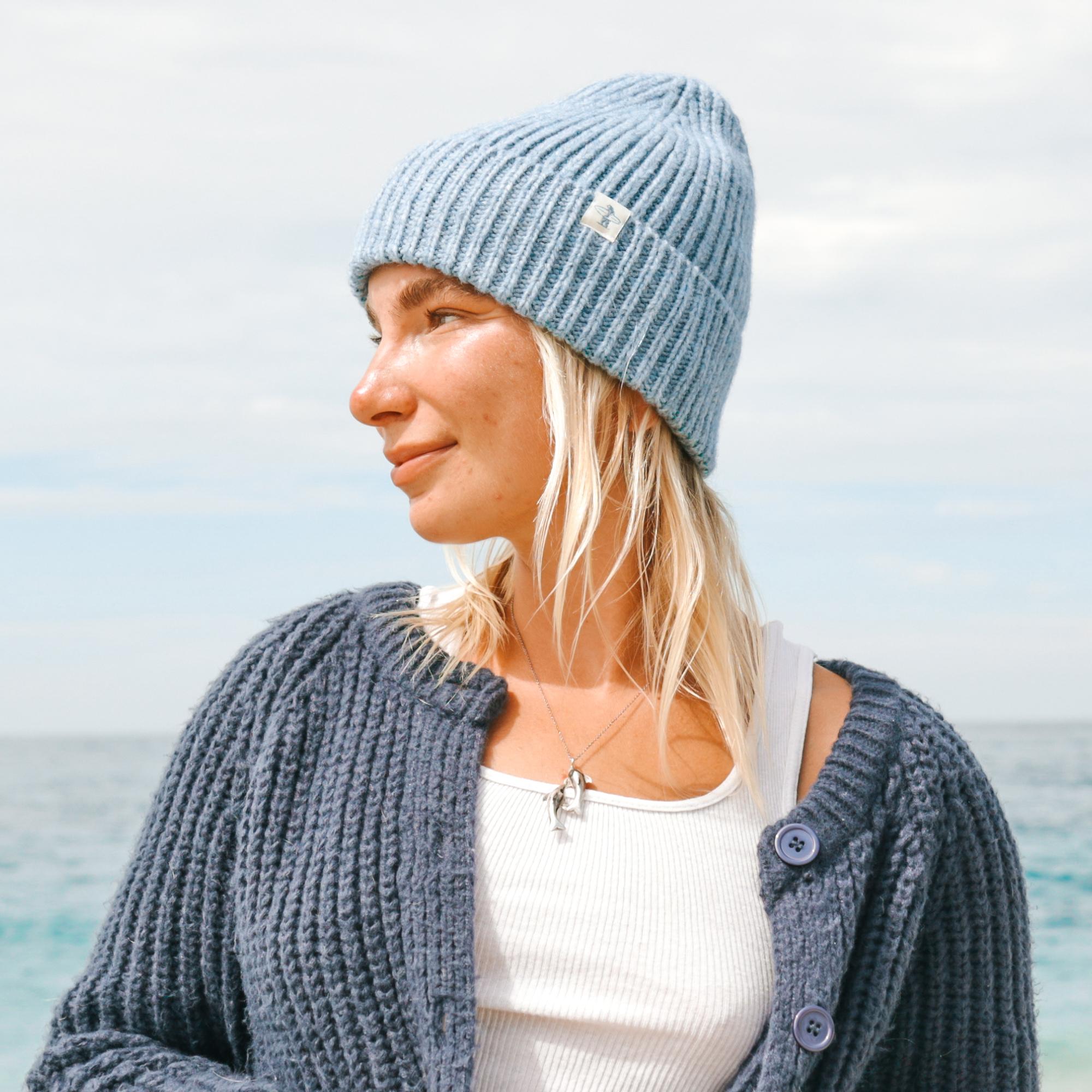 Female model wearing a blue Everyday California beanie with ocean background