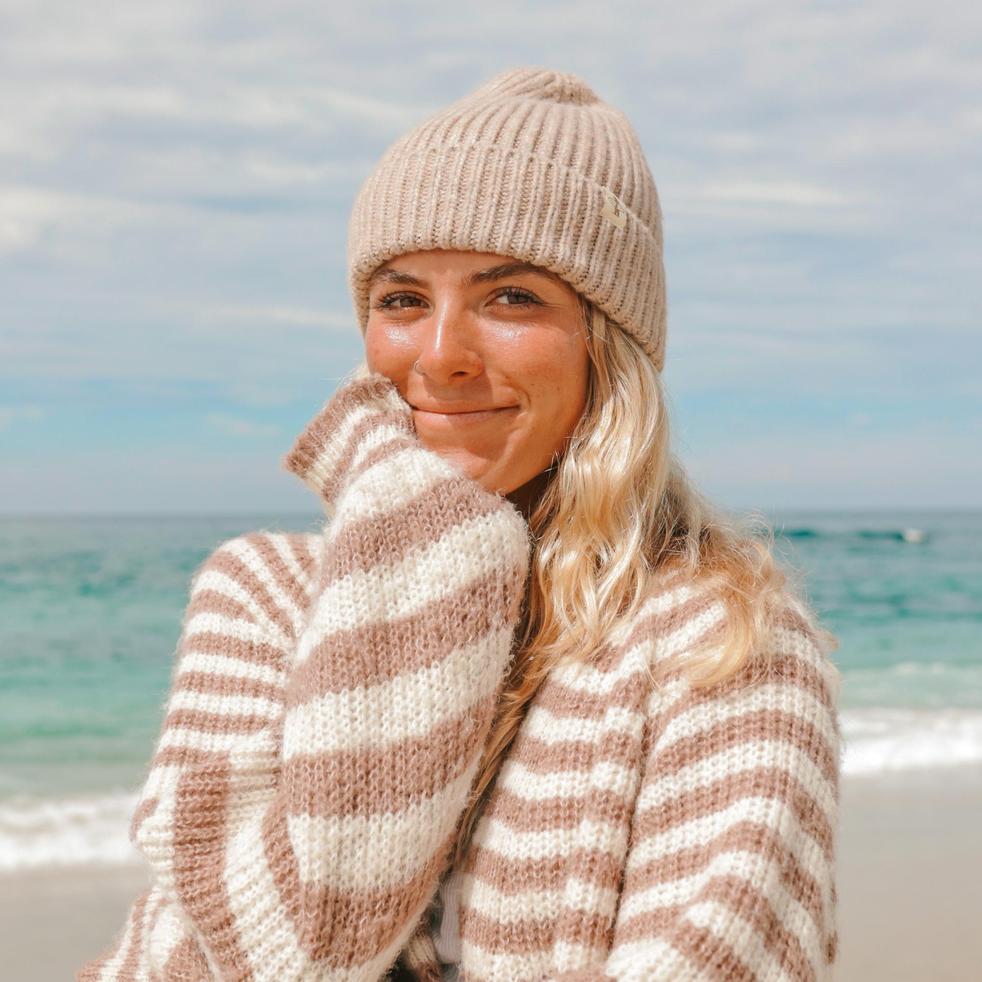 Woman wearing a beige knit hat and striped sweater on a beach