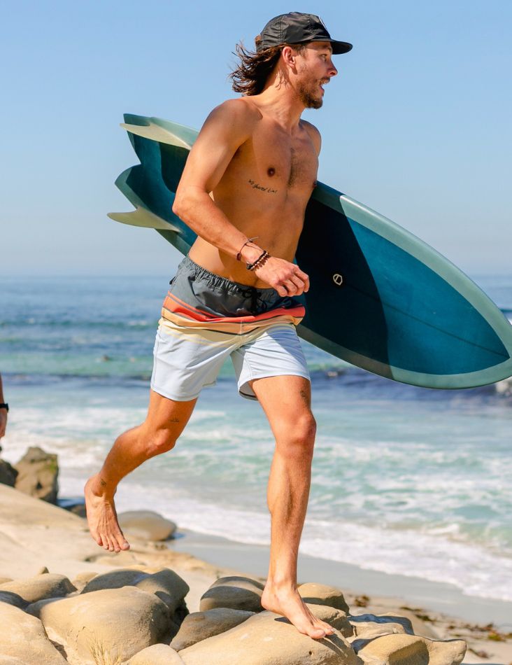 Man walking on rocks with a surfboard at the beach