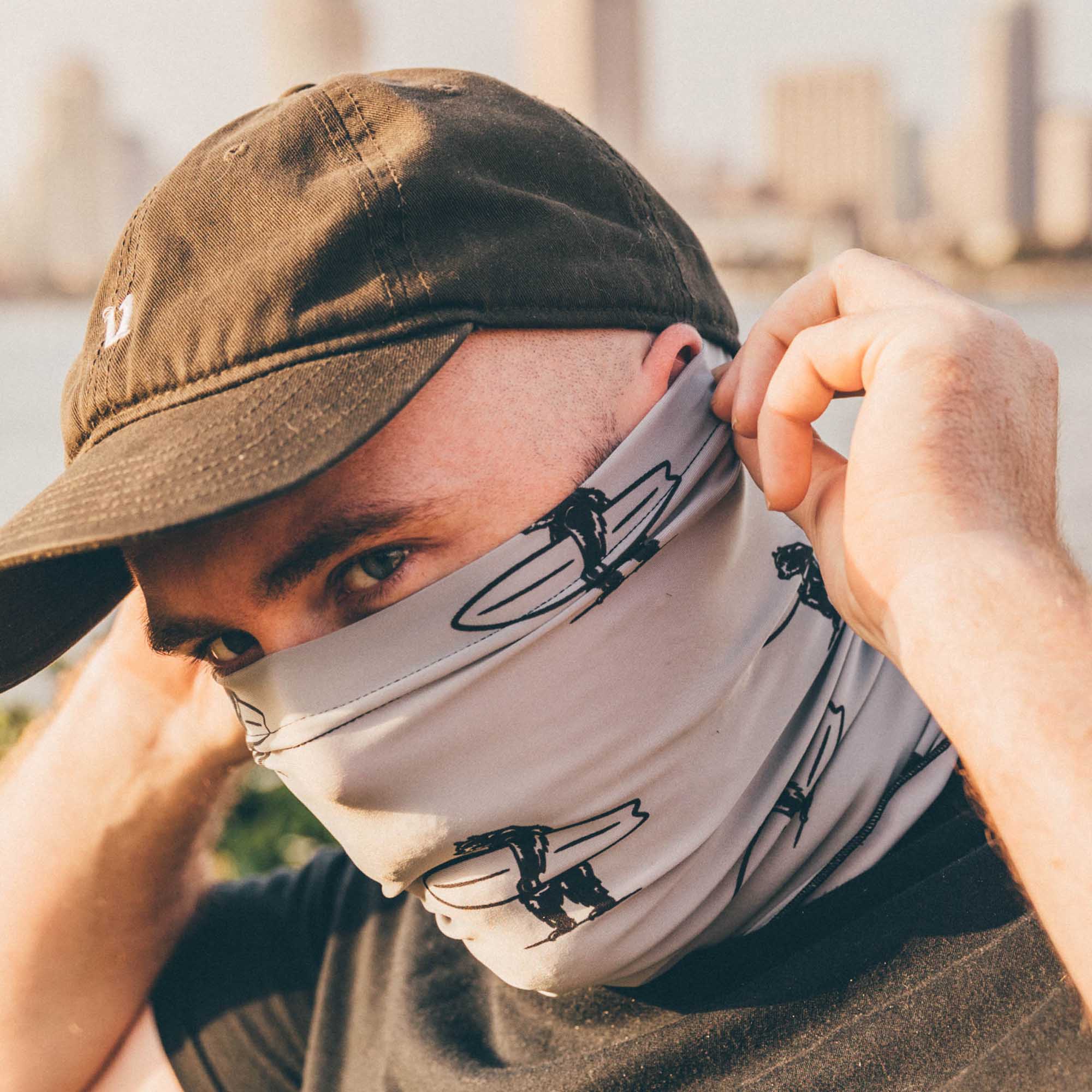 Neck gaiter featuring black logo images of a bear holding a surfboard on a gray background.
